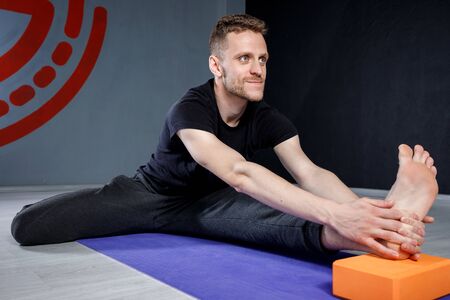 Young man is stretching his leg on yoga mat with yoga brick.の写真素材