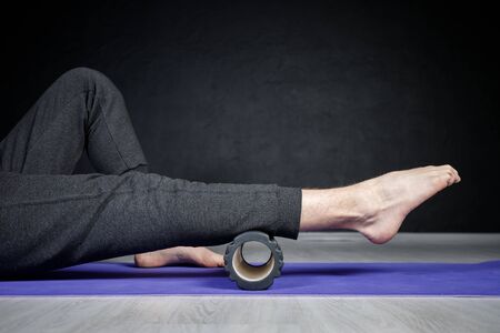 Young athletic man is doing leg stretches with the help of yoga roller.の写真素材