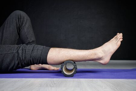 Young athletic man is doing leg stretches with the help of yoga roller.の写真素材