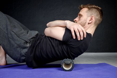 Young athletic man is working out his spine muscles with a roller.の写真素材