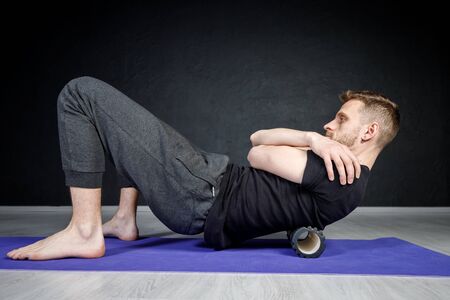 Young athletic man is working out his spine muscles with a roller.の写真素材