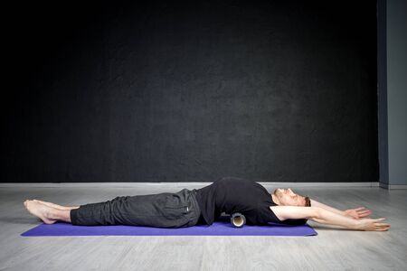 Young athletic man is working out his spine muscles with a roller.の写真素材