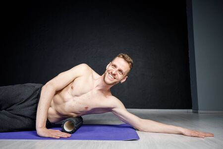 Young athletic man is working out his spine muscles with a roller.の写真素材