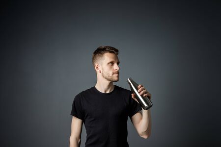 Young man on the black background is drinking water from fitness bottle.の写真素材