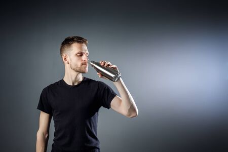 Young man on the black background is drinking water from fitness bottle.の写真素材