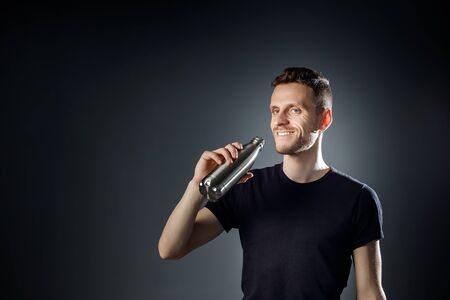 Young smiley man on the black background is drinking water from fitness bottle.の写真素材
