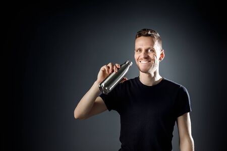 Young smiley man on the black background is drinking water from fitness bottle.の写真素材