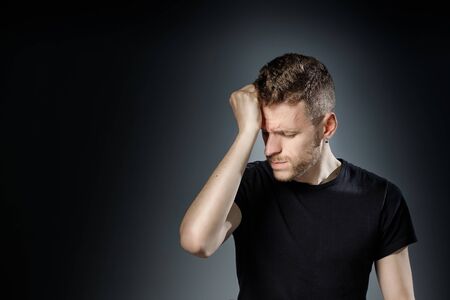 Young man, is having a headache on black background.