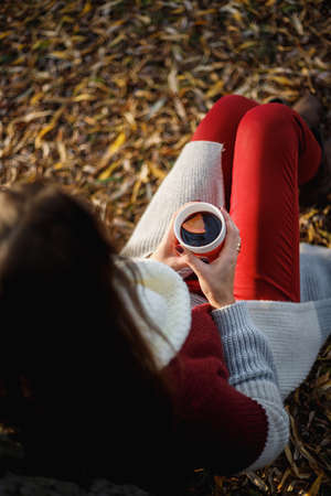 Beautiful woman sitting under a tree with a cup of mulled wine in her hands.