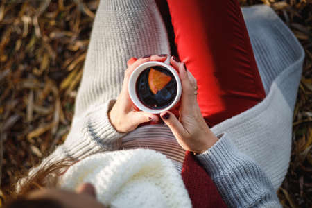 Beautiful woman sitting under a tree with a cup of mulled wine in her hands.の写真素材