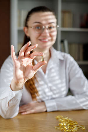 The girl holds a fish oil capsule in her hand. Omega-3 capsules on the table and in the doctor's hand.の写真素材
