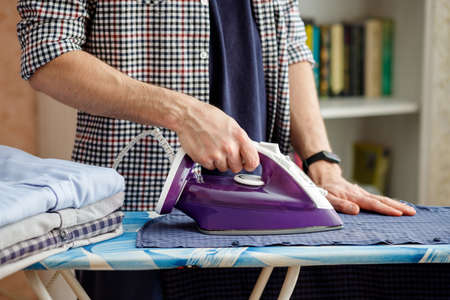 A man irons a shirt on an ironing board with an iron. Daily household chores.の写真素材