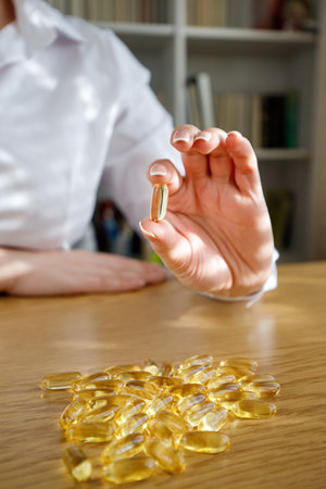 The girl holds a fish oil capsule in her hand. Omega-3 capsules on the table and in the doctor's hand.の写真素材