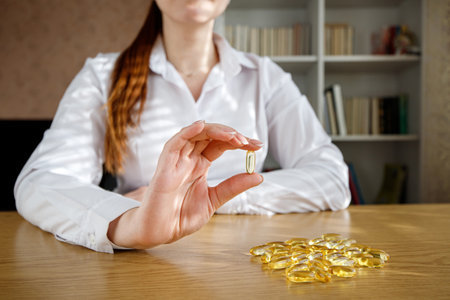 The girl holds a fish oil capsule in her hand. Omega-3 capsules on the table and in the doctor's hand.の写真素材