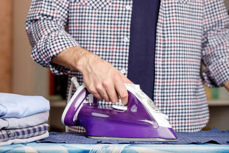 A man irons a shirt on an ironing board with an iron. Daily household chores.の写真素材