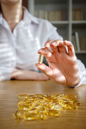 The girl holds a fish oil capsule in her hand. Omega-3 capsules on the table and in the doctor's hand.の写真素材
