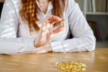 The girl holds a fish oil capsule in her hand. Omega-3 capsules on the table and in the doctor's hand.の写真素材
