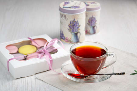 Multicolored macaroons in a box and a cup of tea on a light wood kitchen table. Morning tea and sweets.の写真素材