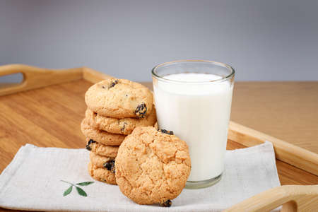 A glass of milk and cookies with raisins on a wooden trayの写真素材