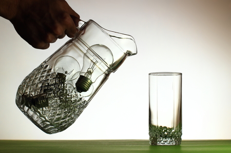 Hand pouring from jug of light bulbs into glassの写真素材