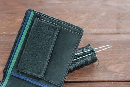 Men's black leather wallet on wooden boards and threads, needles.