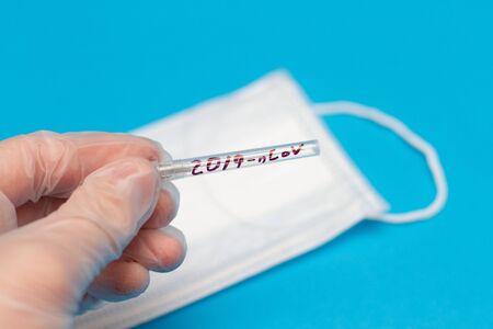 New coronavirus, needle test tube with the inscription 2019-nCoV on hand with respiratory mask on blue backgroundの写真素材