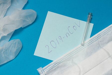 Novel coronavirus disease called 2019-nCoV handwriting on blue paper. protective mask and surgical gloves on blue background