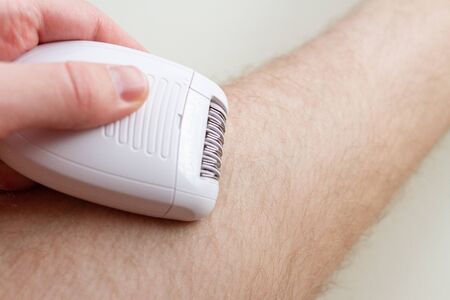 Men epilates his leg with an electric epilator deviceの写真素材