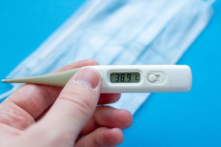 digital thermometer in hand with high body temperature. Medical mask and thermometer. 38.9 on...