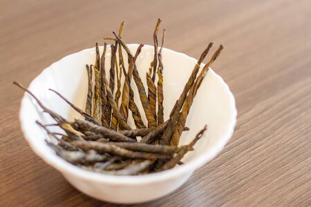 Dry tea with green leaves in white plate, on wooden background.の写真素材