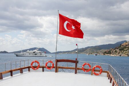 Flag of Turkey on a ship at sea on a background of mountains and a luxury yacht.