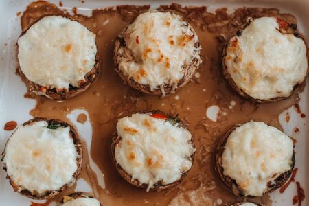 Baked Champignons with cheese and vegetables stuffed on a white plate. Top view.
