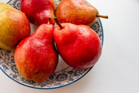 Red ripe pears with drops of water in a white plate with a blue pattern on a white backgroundの写真素材