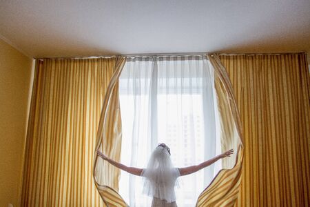 Bride in a wedding dress opens the curtains.