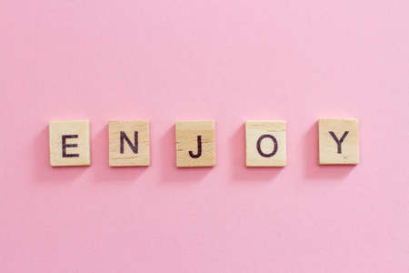 Wooden cubes inscription Enjoy on pink background.