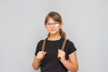 Cute little schoolgirl in eyeglasses with backpack smiling at camera.の写真素材