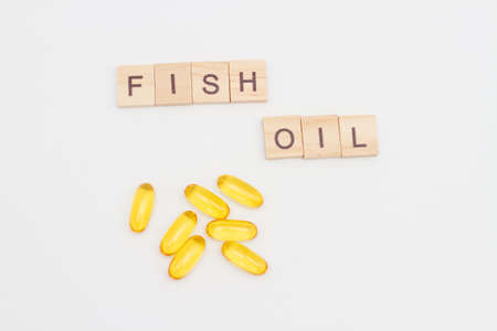 Wooden blocks with letters and words FISH OIL and capsules with fish oil and omega 3 on white background.の写真素材