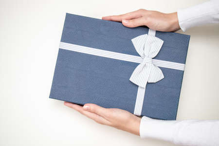 Women's hands hold a holiday blue gift box with bow for present. Flat lay style.