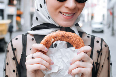 Cute young woman holding in hand traditional Turkish simit in a female hand. Crispy bagel with sesame seedsの写真素材