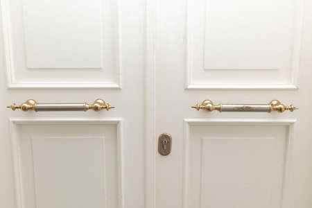 White wood front door with golden retro handles and keyhole closeup.の写真素材