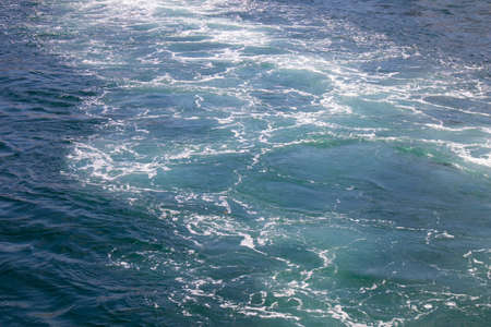 Green clear sea water background surface with small white foam waves.