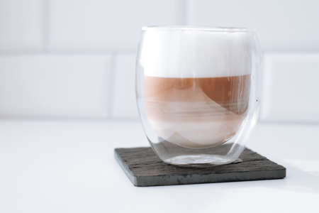 Cappuccino coffee in a double glass on a black slate board against white bricks wall background.の写真素材
