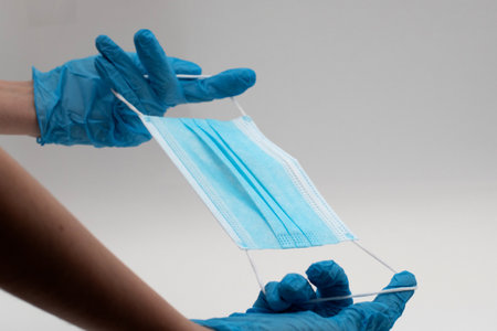 Doctors hand dressed in the blue medical gloves with a medical face mask for protection.