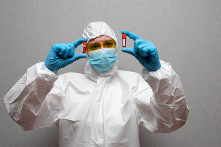 Woman doctor in protective suit and mask holding virus infected blood sample test tube.の写真素材
