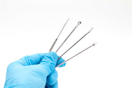 Doctor's hand in a blue glove holds Acne removal tools.の写真素材