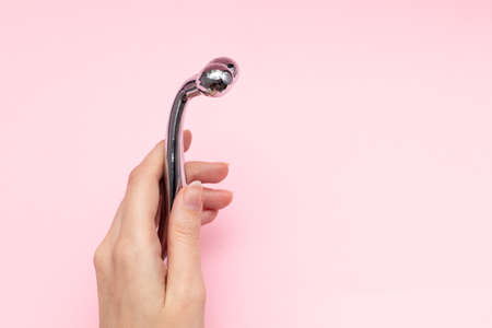 Female hand holding silver massage roller for facial massage on pink backgroundの写真素材