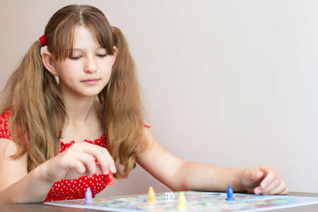 Smiling child girl in red dress playing board game at home. Board game field. Selective focus.