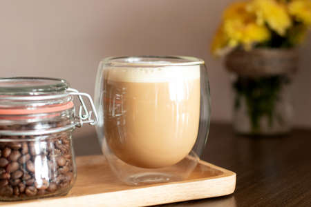 Cappuccino in a double glass cup and jar with coffee beans on wooden plate