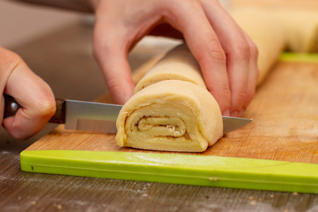 Woman's hands cut the roll of dough. Pastry chef cuts the rolls of dough. The process of making buns.の写真素材