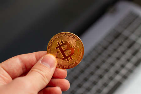 Man holding Bitcoin in hand near laptop.の写真素材